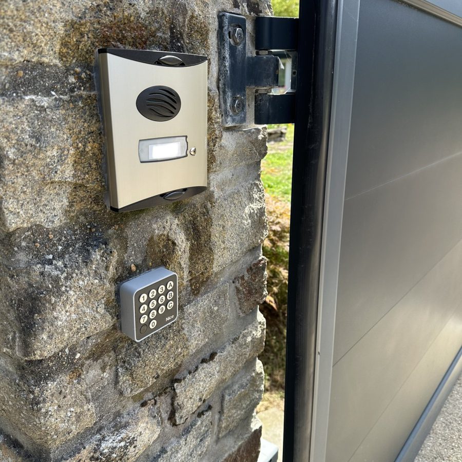 Interphone et clavier à code installés sur un pilier en pierre, à côté d'un portail