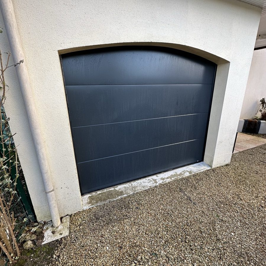 Porte de garage sectionnelle anthracite posée dans une ouverture cintrée